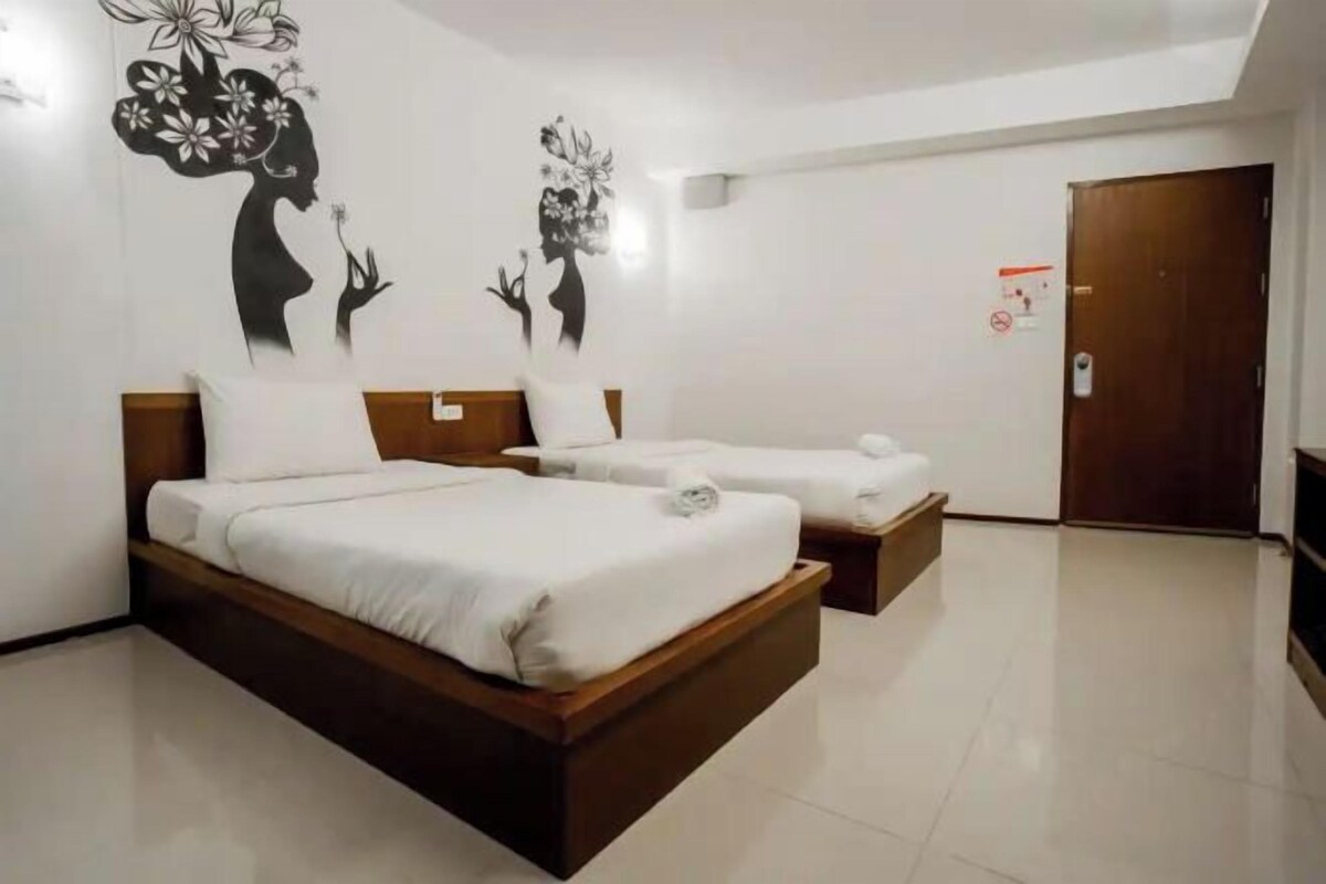 A hotel room with two beds, a wooden headboard, a white tiled floor, and wall art depicting floral designs.