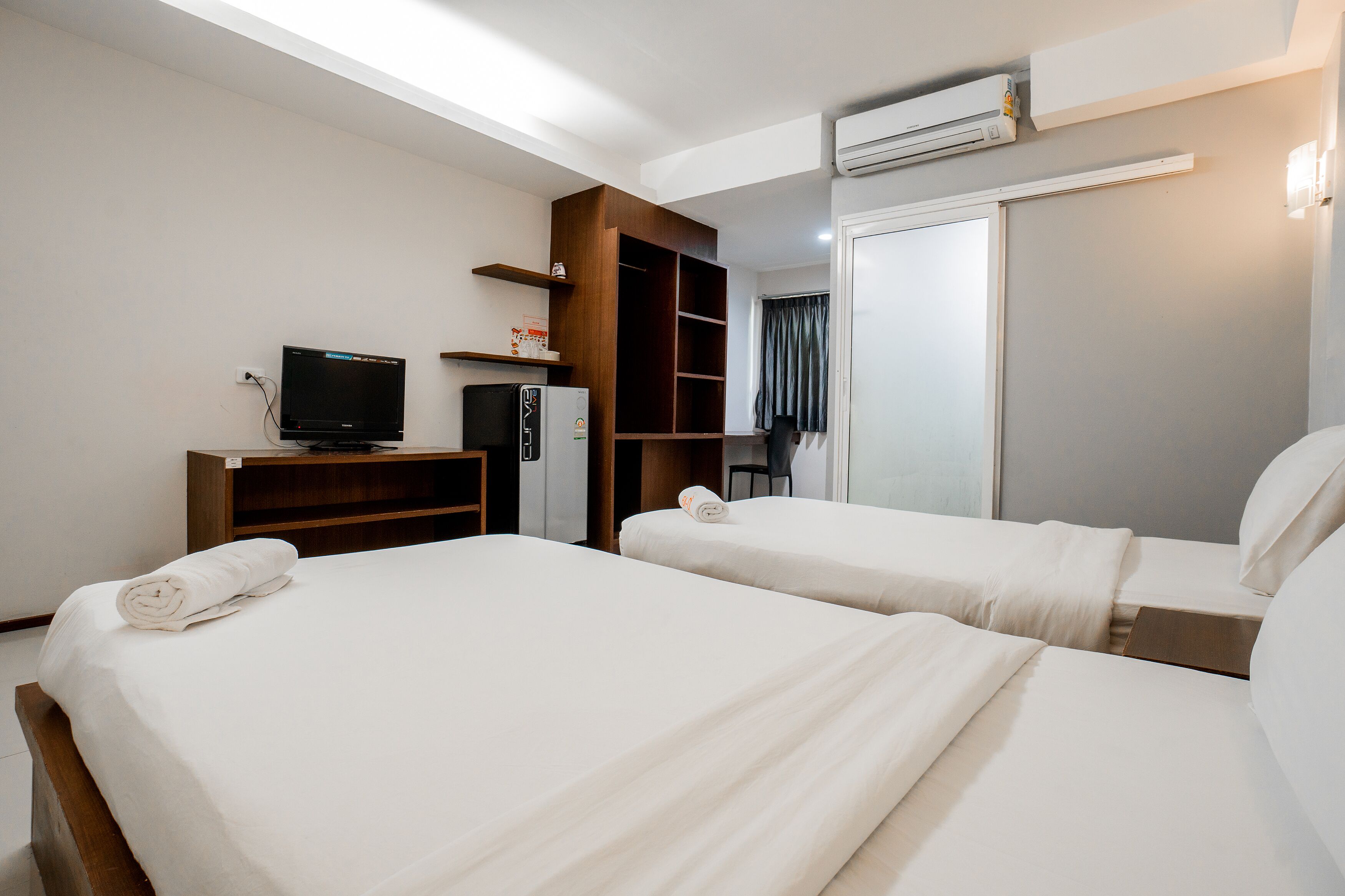 Ein Hotelzimmer mit zwei Betten, einem Fernseher, einer Minibar, einem Kleiderschrank und einem Spiegel.