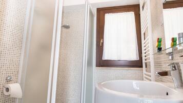 A bathroom with a glass shower enclosure, a sink with a mirror, and a window with curtains.