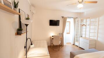 Ein Schlafzimmer mit Bett, Nachttisch, Lampe, Fernseher, Schreibtisch, Stuhl, Kleiderschrank und Deckenventilator.