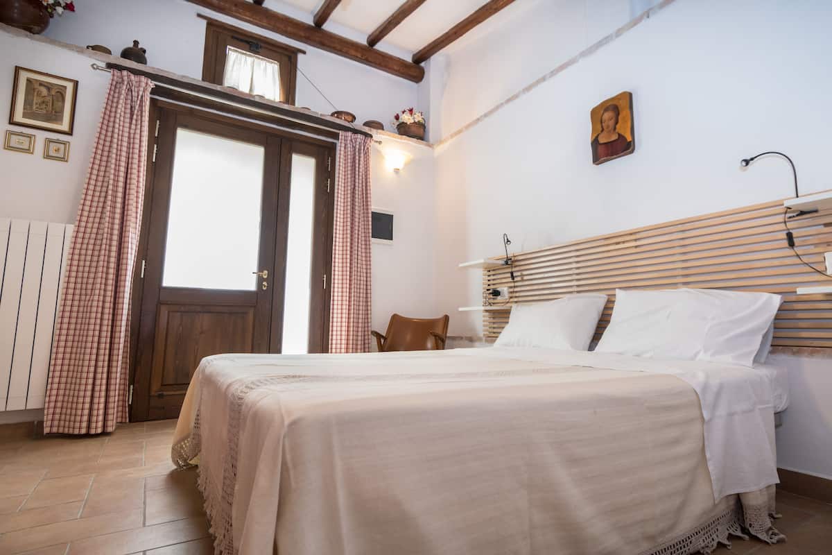 Quarto com cama, cadeira, cabeceira de madeira, porta e janela com cortinas.