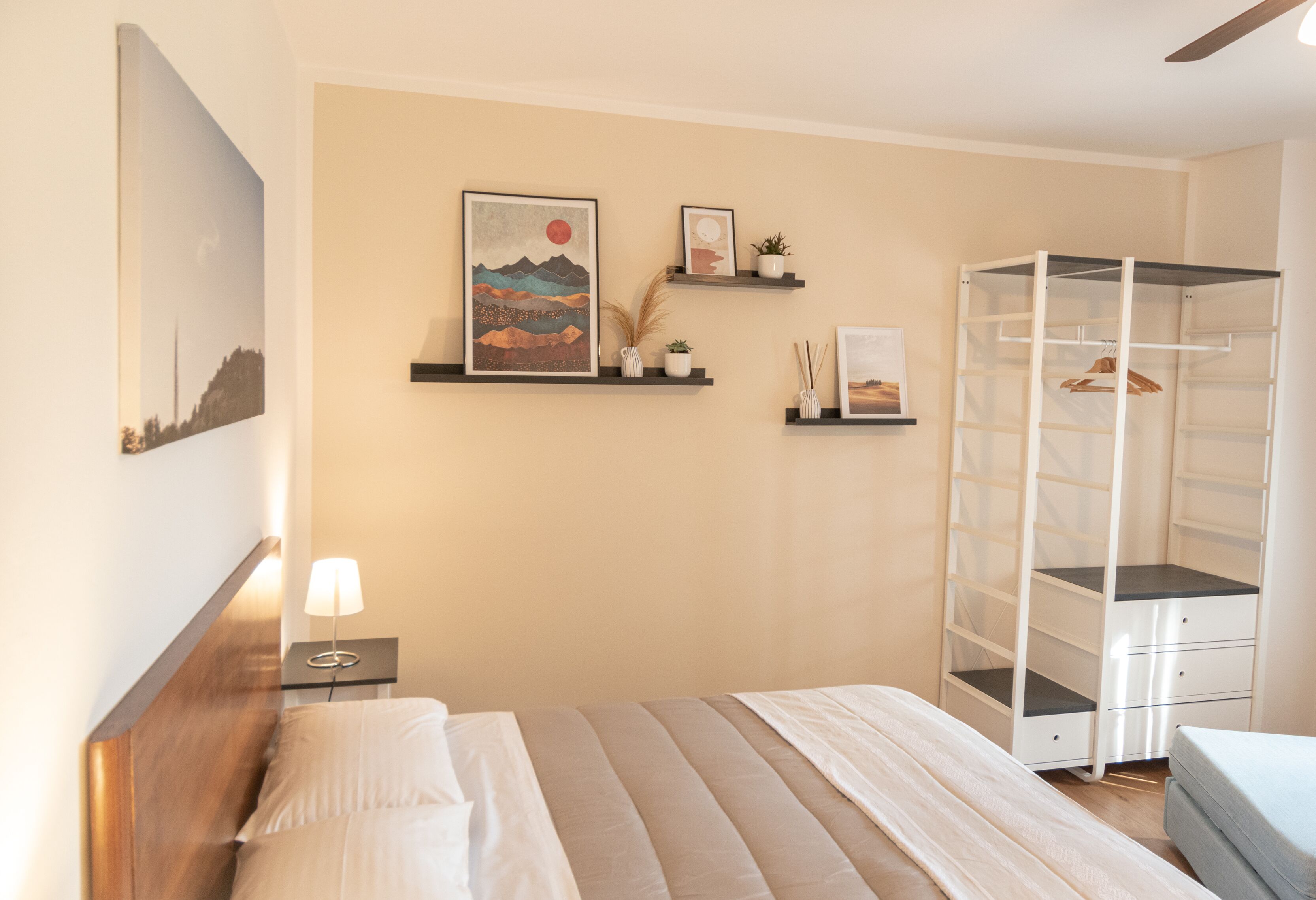 A bedroom with a bed, a nightstand, a wall-mounted shelf with decorative items, and a built-in wardrobe.