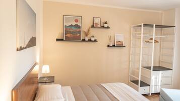 A bedroom with a bed, a nightstand, a wall-mounted shelf with decorative items, and a built-in wardrobe.