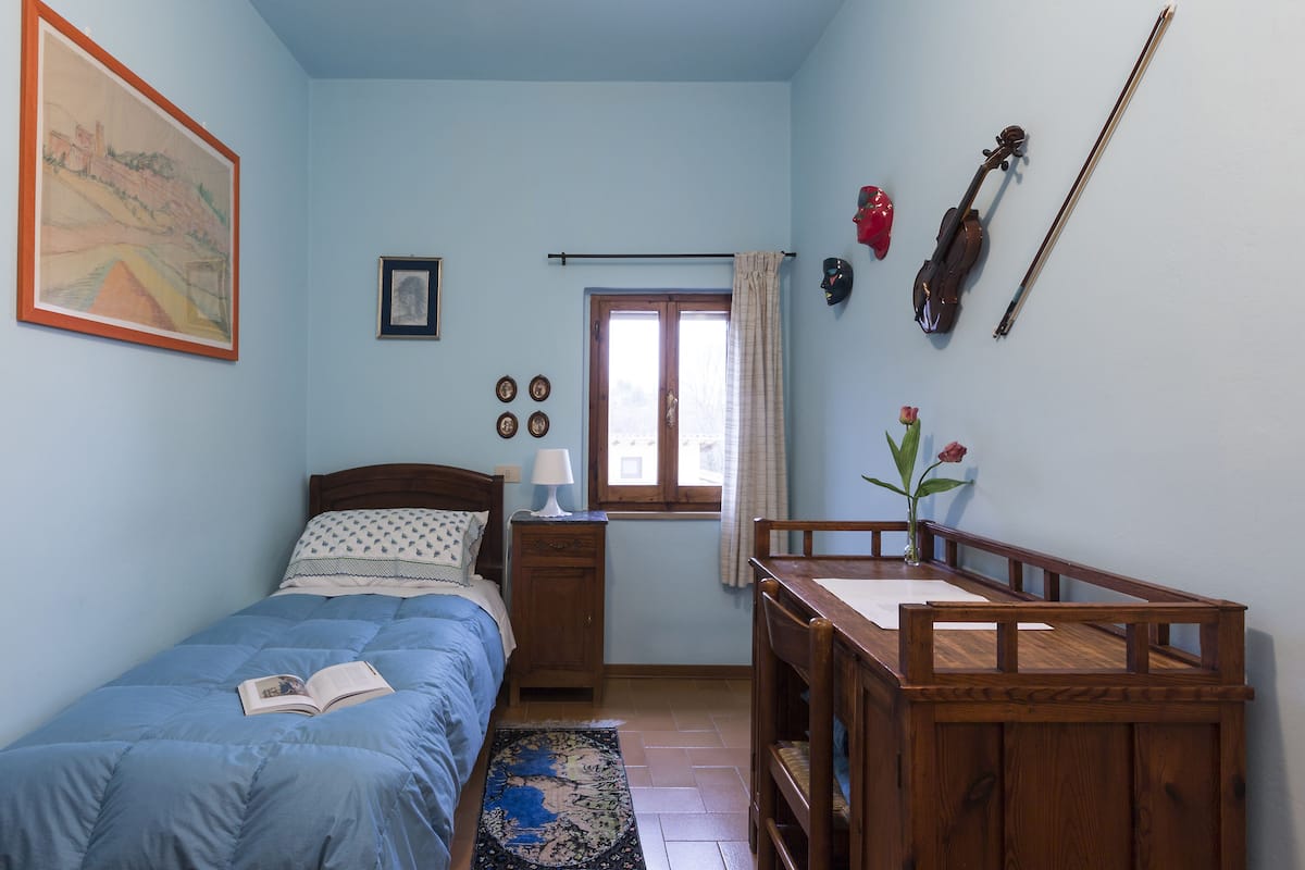 Quarto com cama, mesa de cabeceira e escrivaninha de madeira com cadeira.