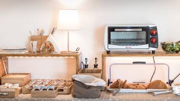 A kitchen with a Girmi toaster oven, a wooden table with a lamp, and various kitchen items.