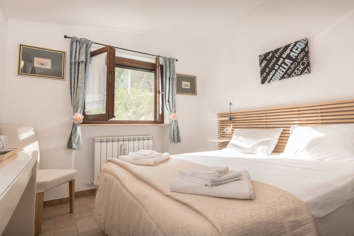 Quarto bem arrumado com cama, uma cadeira, radiador e janela com cortinas.