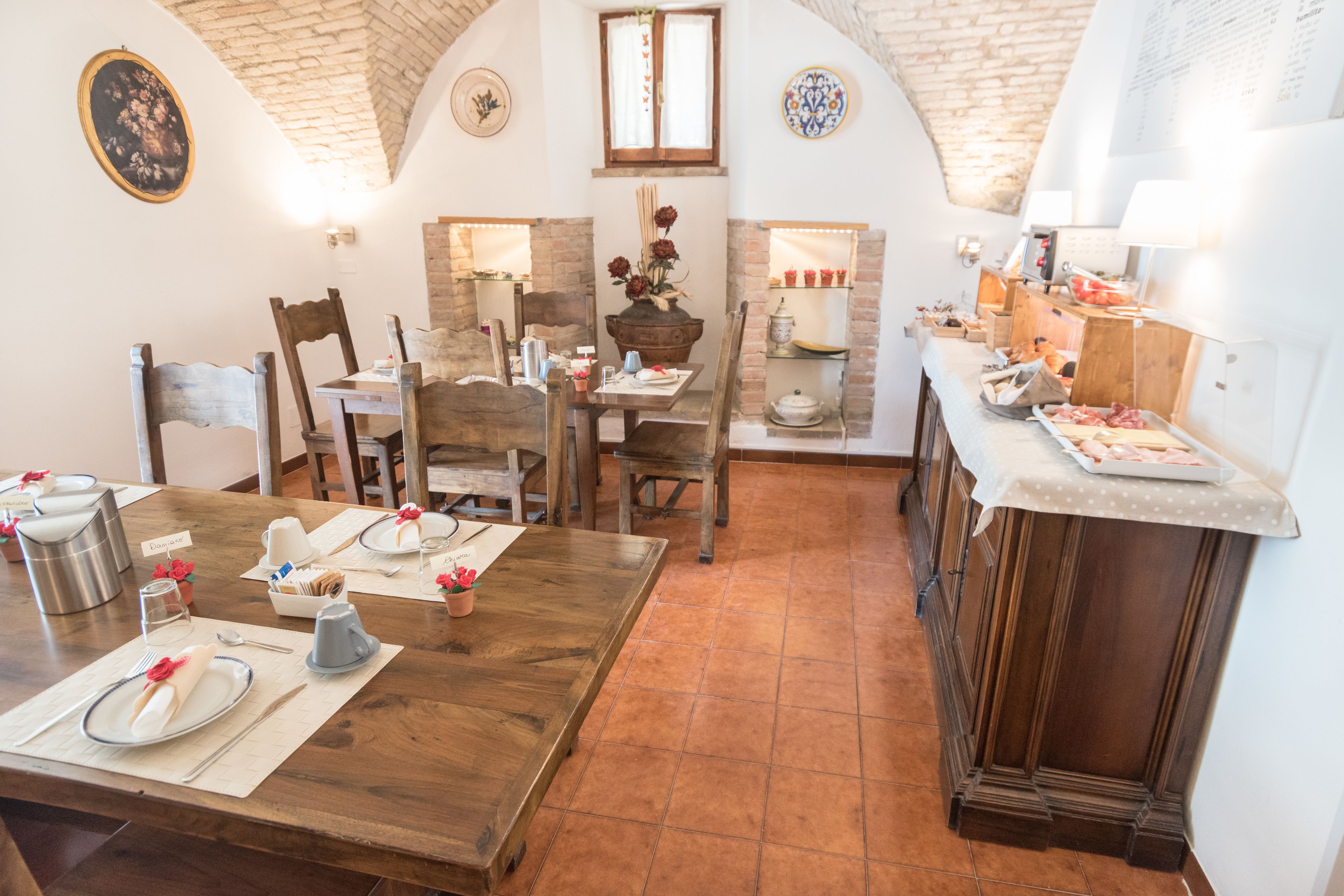 A dining area with wooden tables and chairs, a kitchen with a brick wall, and a small window.