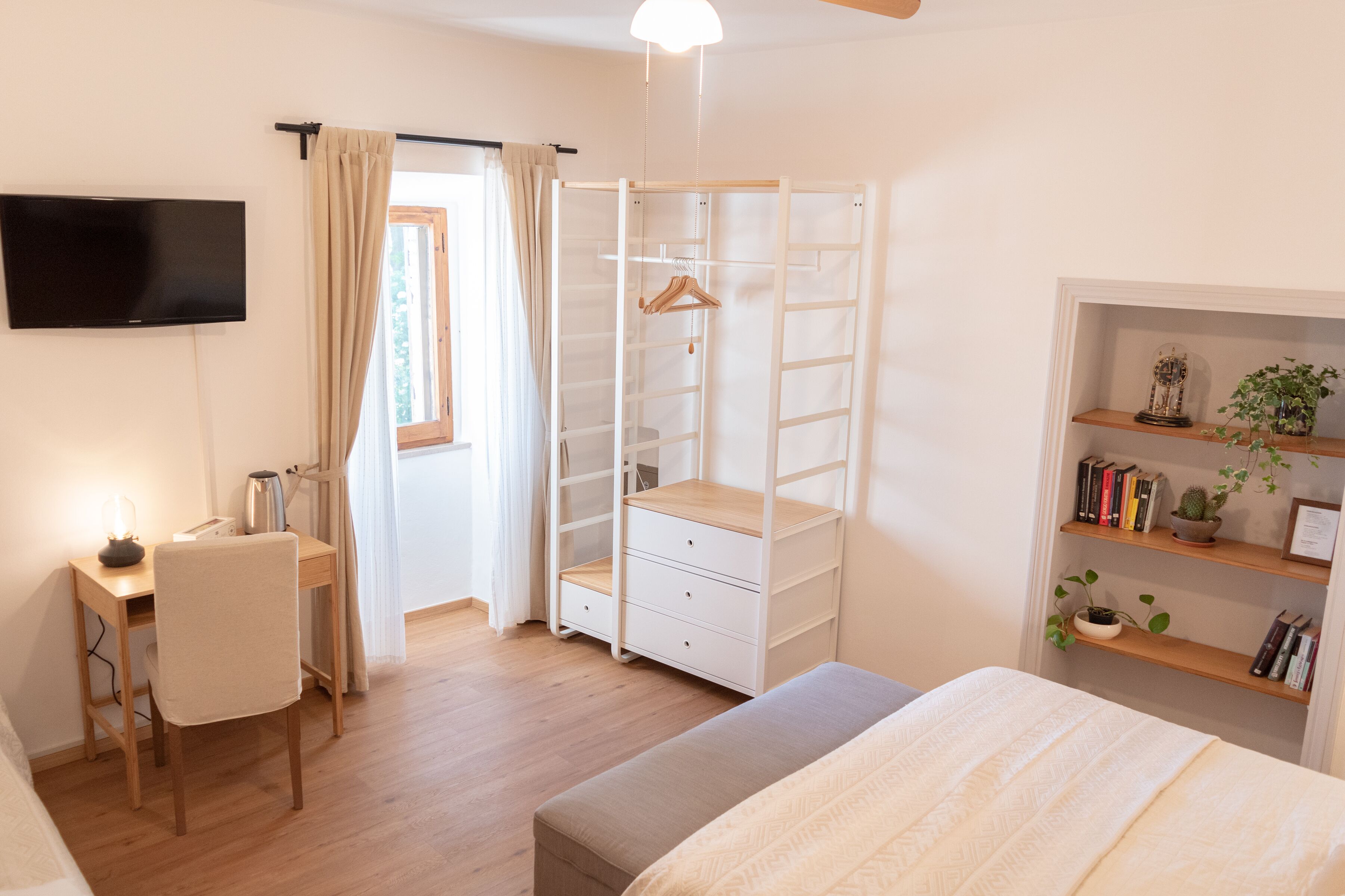 Un dormitorio con cama, escritorio y silla, armario y televisor montado en la pared.