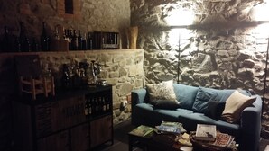 A cozy living room with a stone wall, a blue sofa, and a wooden cabinet with bottles. - Tananei (Marliana)