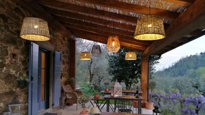 An outdoor patio with wicker lamps, a table with chairs, and a view of a hillside. - Tananei (Marliana)