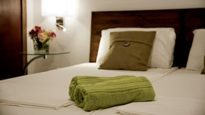 A neatly made bed with a green towel, a wooden headboard, and a bedside table with a vase of flowers. - Marco Polo Malta Hostel (St. Julian's)