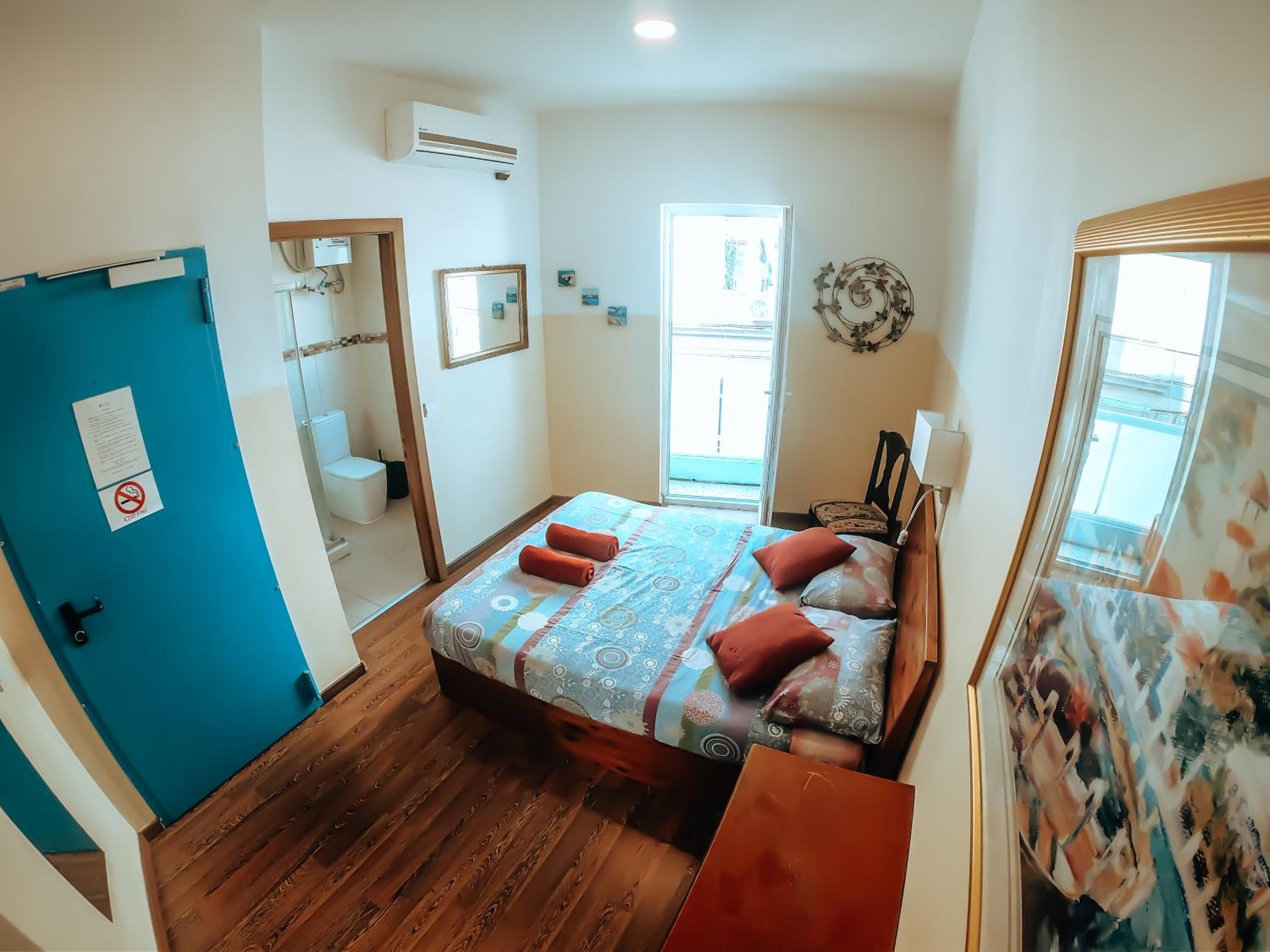 A bedroom with a bed, a window, a door, and a bathroom visible through an open door.