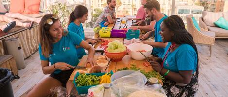 A group of people dining on a rooftop terrace with various food items and a city view in the background.