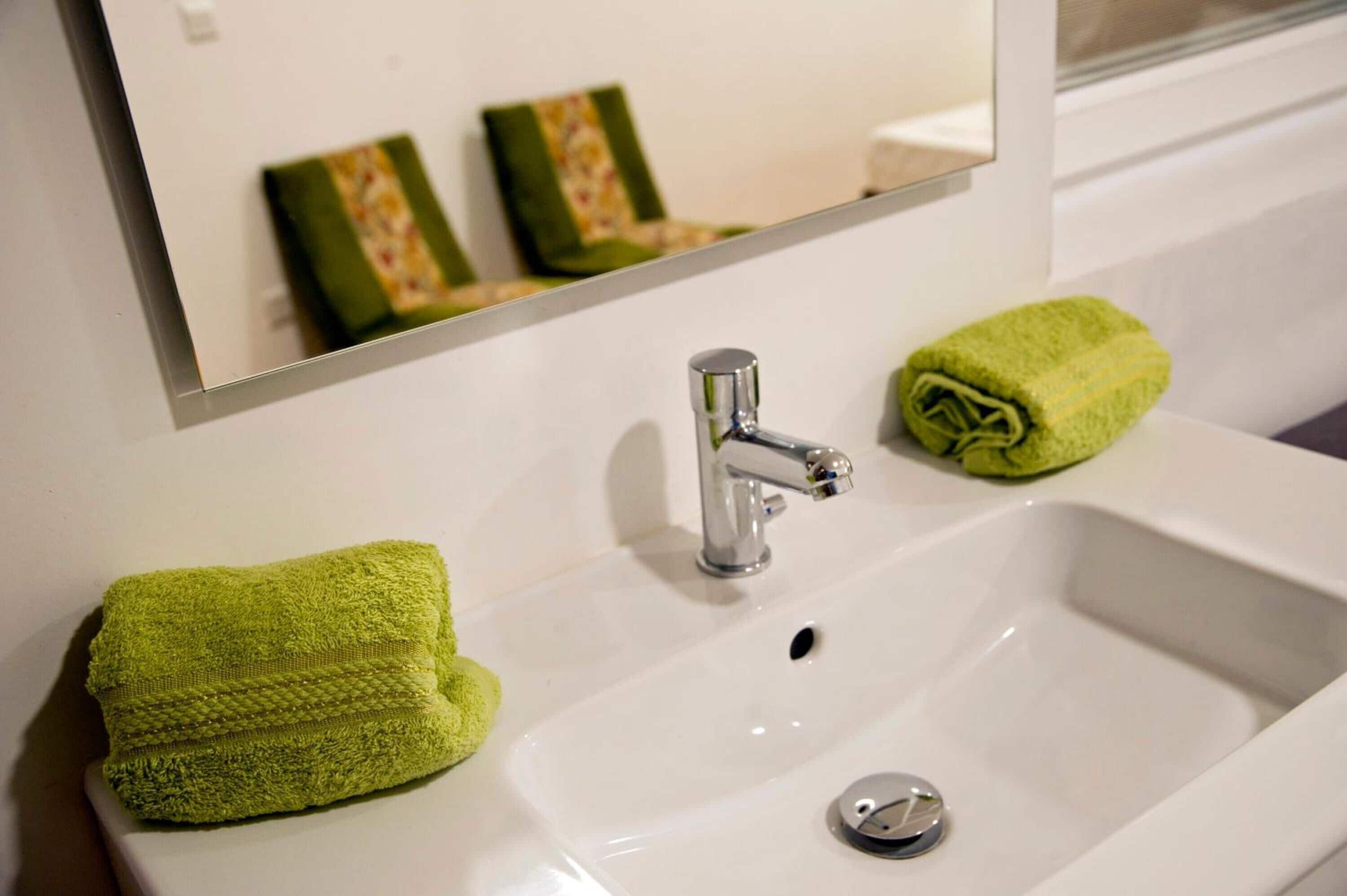 Een badkamer met een witte wastafel, een chromen kraan en twee groene handdoeken op het aanrecht.