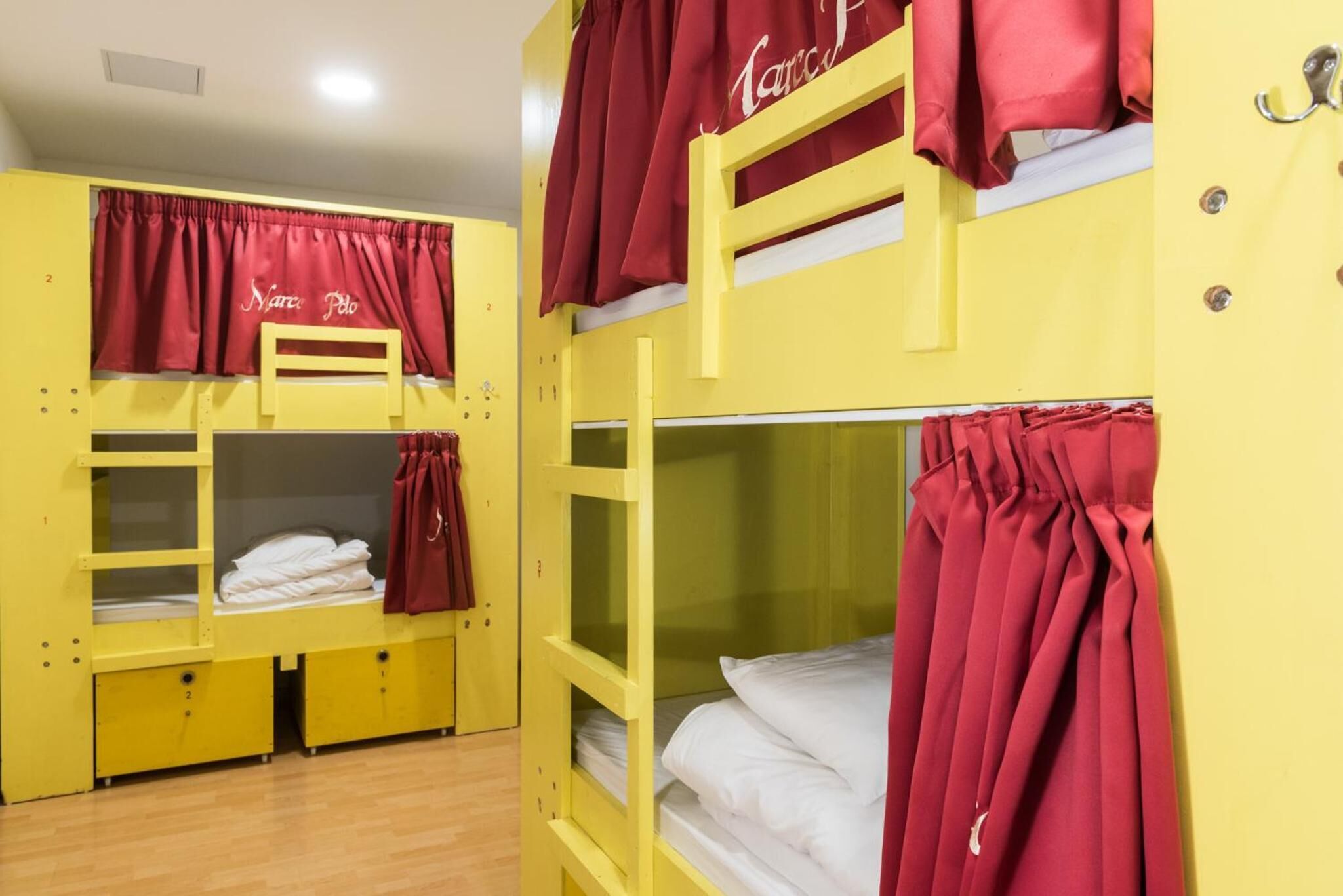 A dormitory room with bunk beds, red curtains, and a visible door handle.