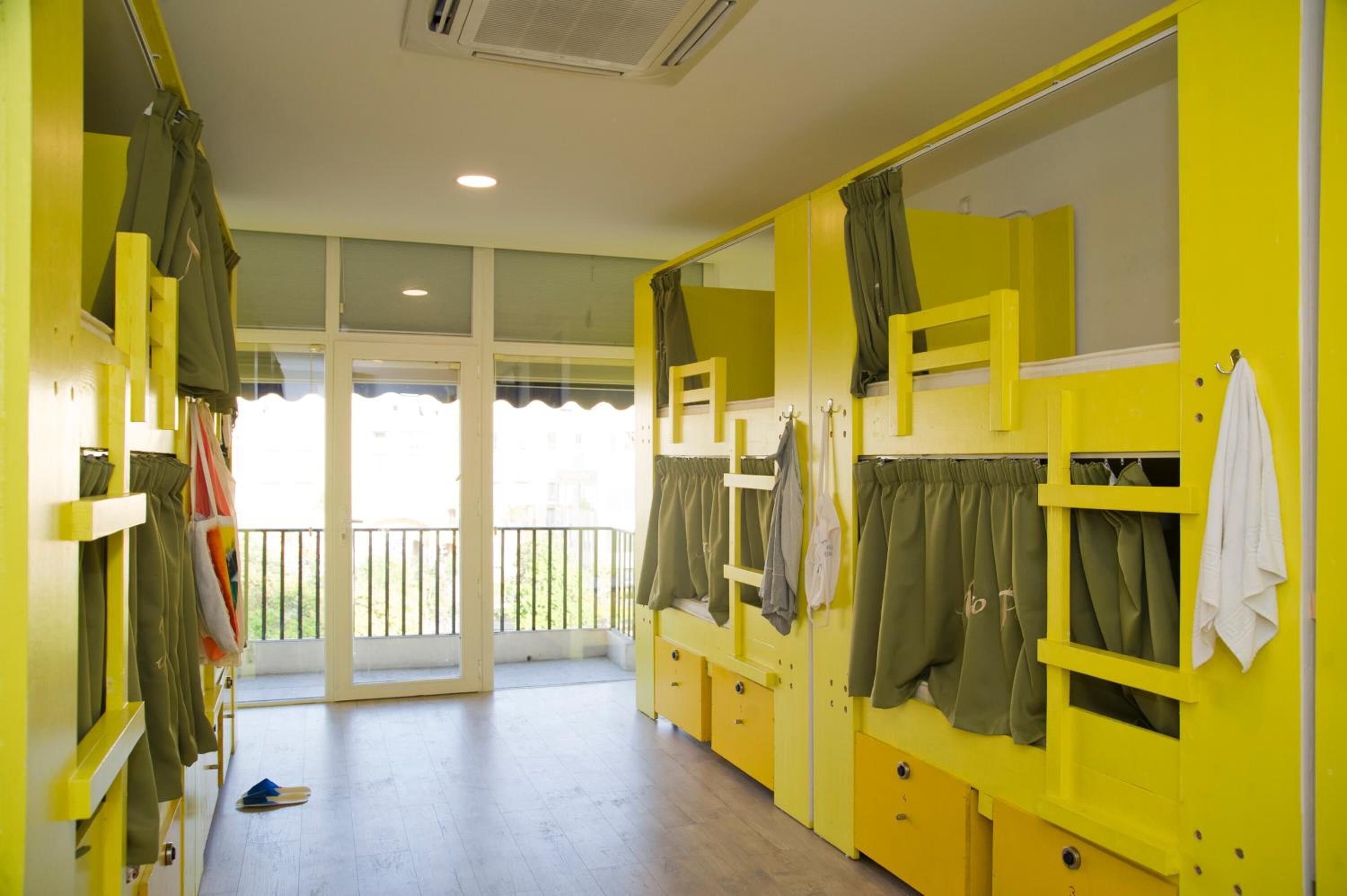 A dormitory room with bunk beds, a balcony, and a large window.
