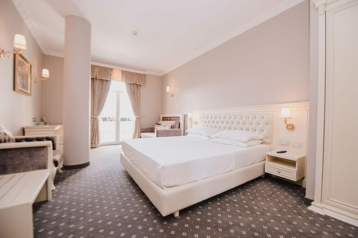 Una habitación de hotel con una cama grande, un escritorio, una silla y una ventana con cortinas.