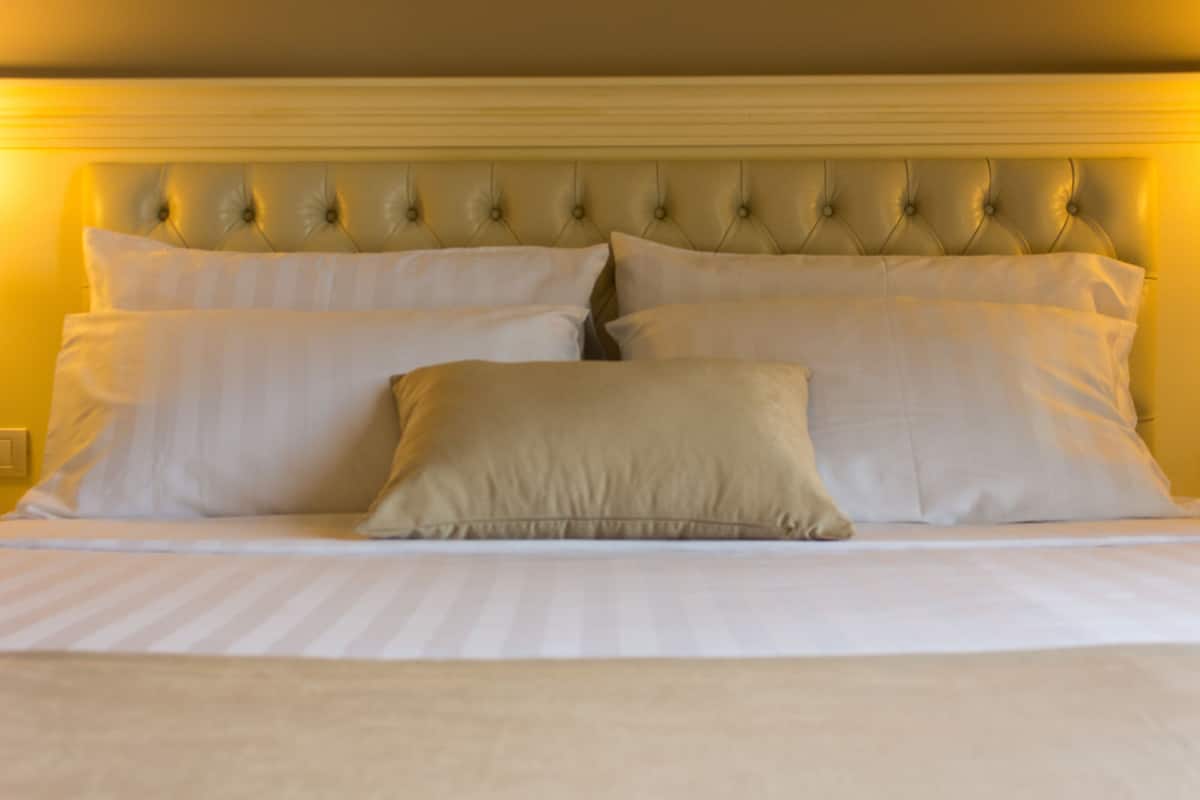 Una cama con cabecera capitonada, varios almohadones y una colcha a rayas.