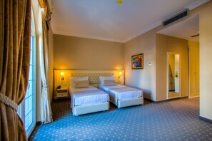 A hotel room with two single beds, a nightstand, a wall-mounted lamp, and a door leading to another room. - Lot Boutique Hotel (Tirana)
