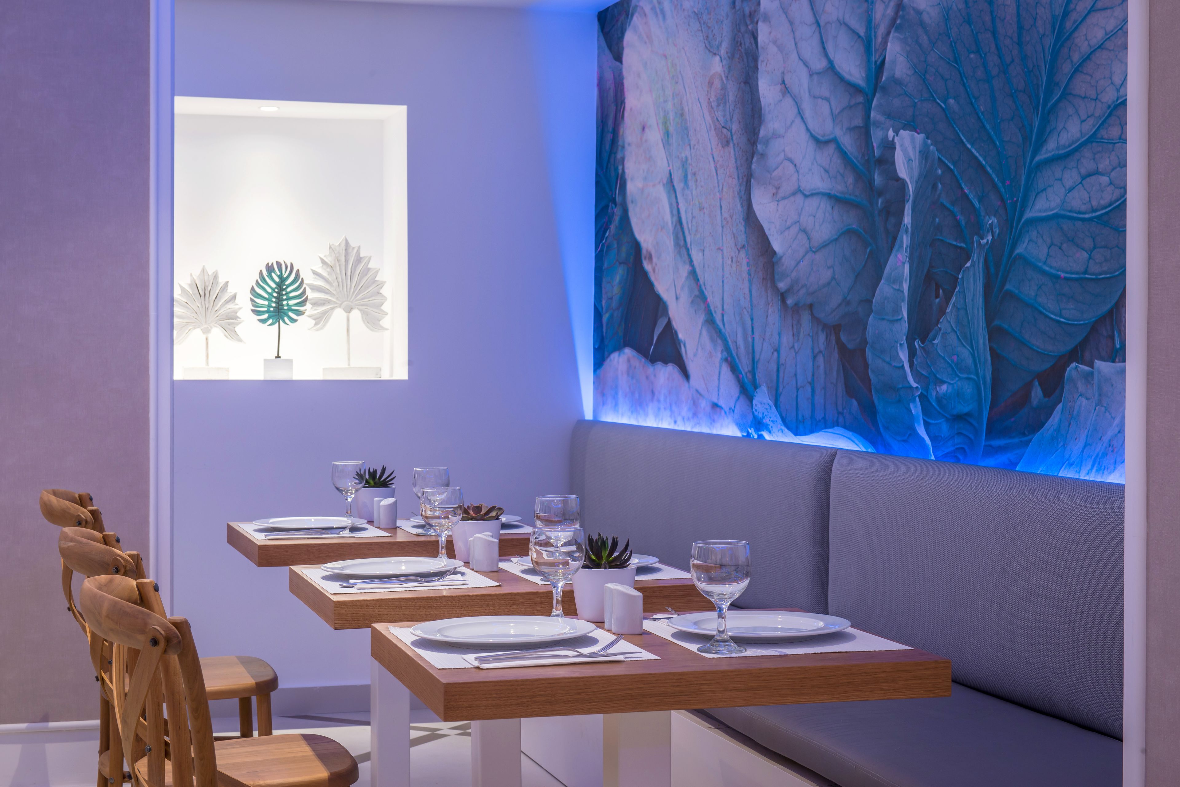 Un comedor con una mesa larga preparada para cuatro personas, un banco y un cuadro abstracto grande en la pared.