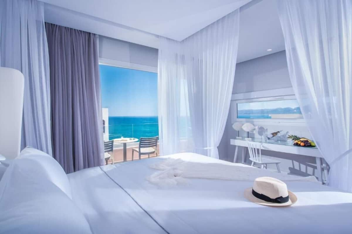 A hotel room with a large bed, a dining table, and a view of the ocean.