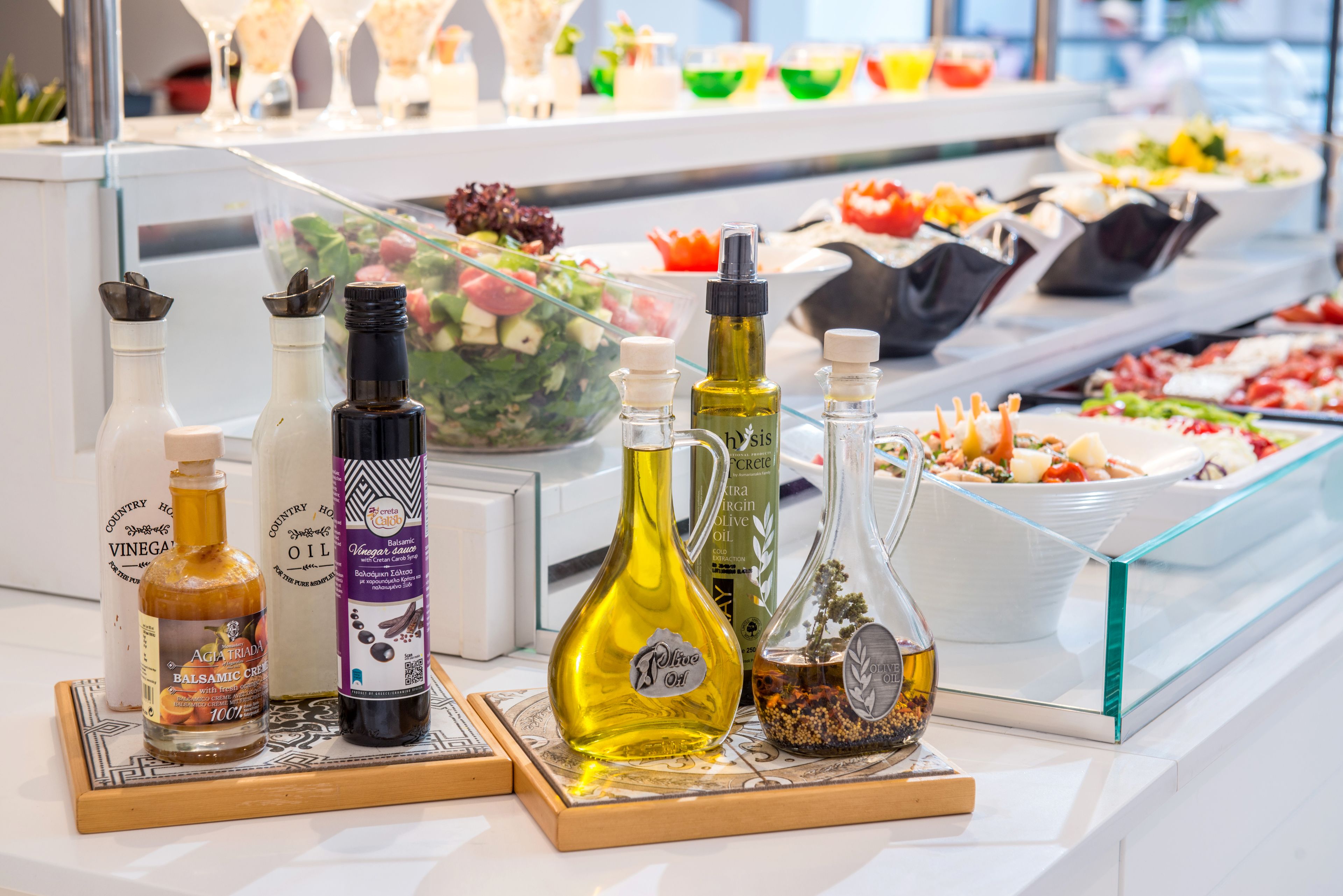 A selection of olive oil bottles on a counter with various food items in the background.