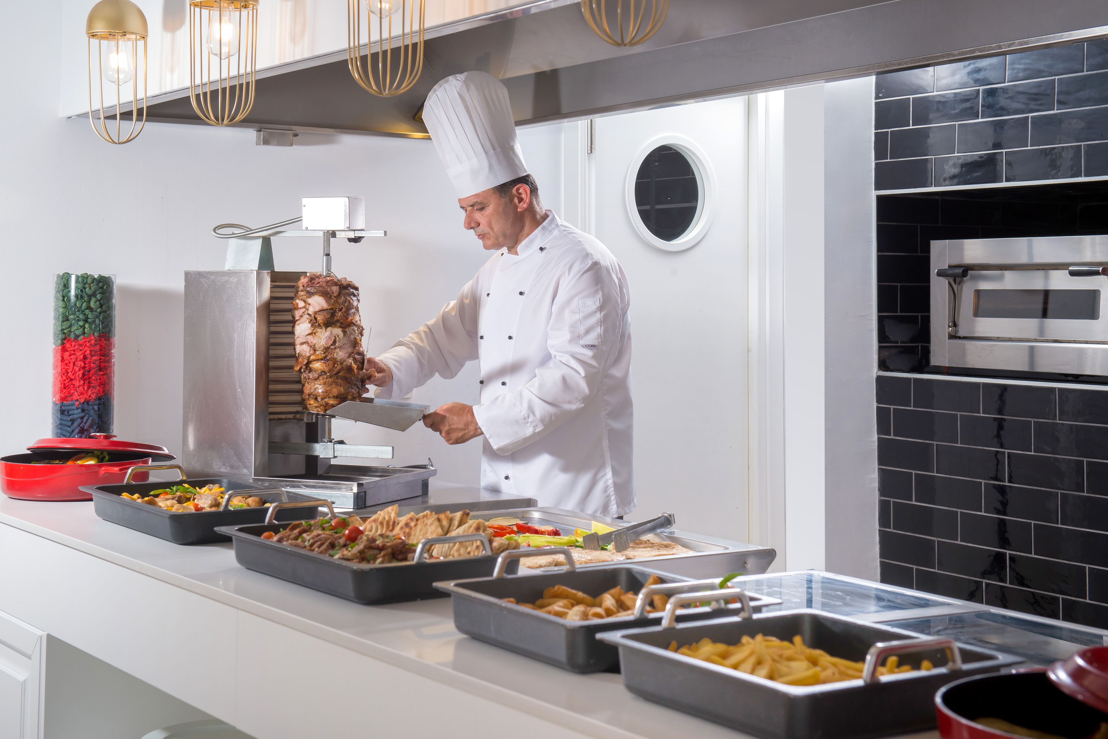 A chef preparing food in a modern kitchen with a meat carving station, buffet-style food service, and a built-in oven.