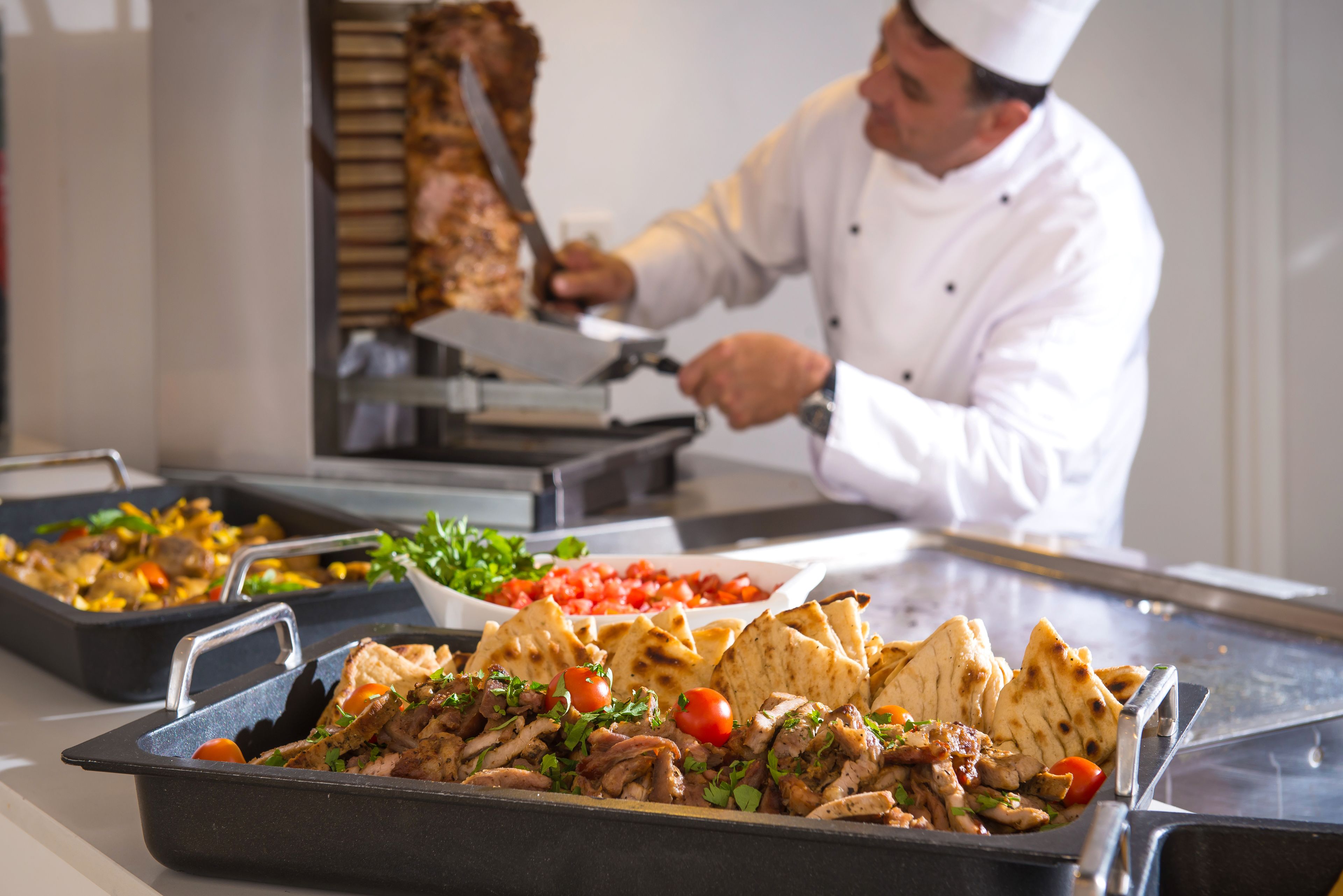A chef preparing food in a kitchen with various dishes and a meat carving station.