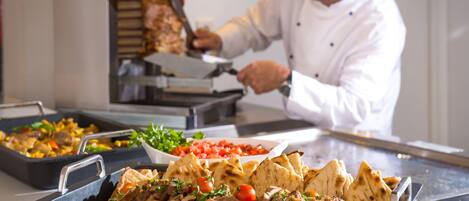 A chef preparing food in a kitchen with various dishes and a meat carving station.