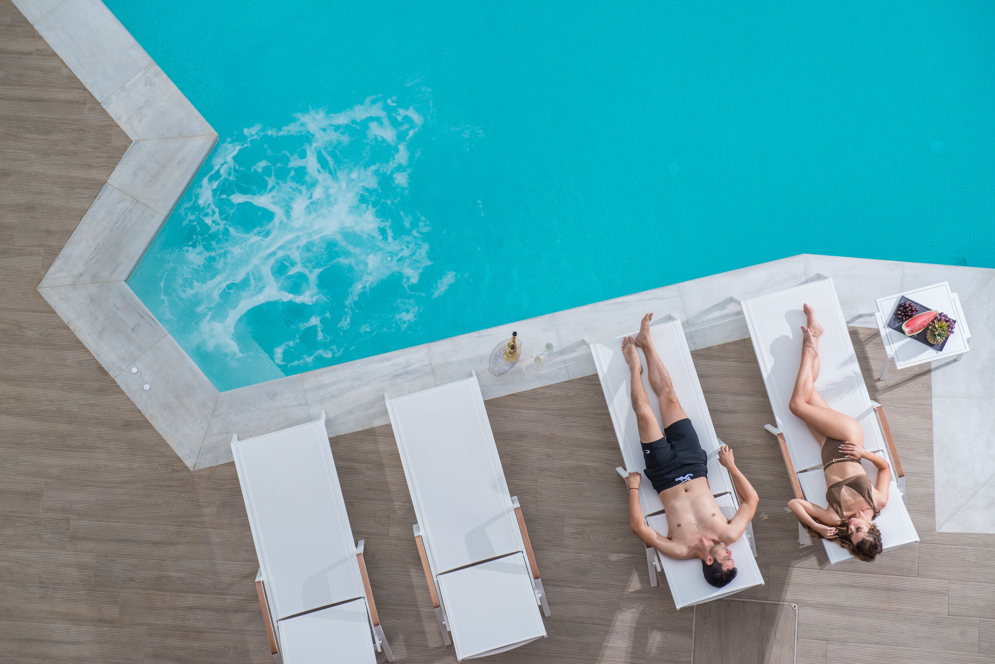 Un espace aménagé au bord de la piscine, avec des chaises longues et une petite table sur laquelle est posée une boisson.