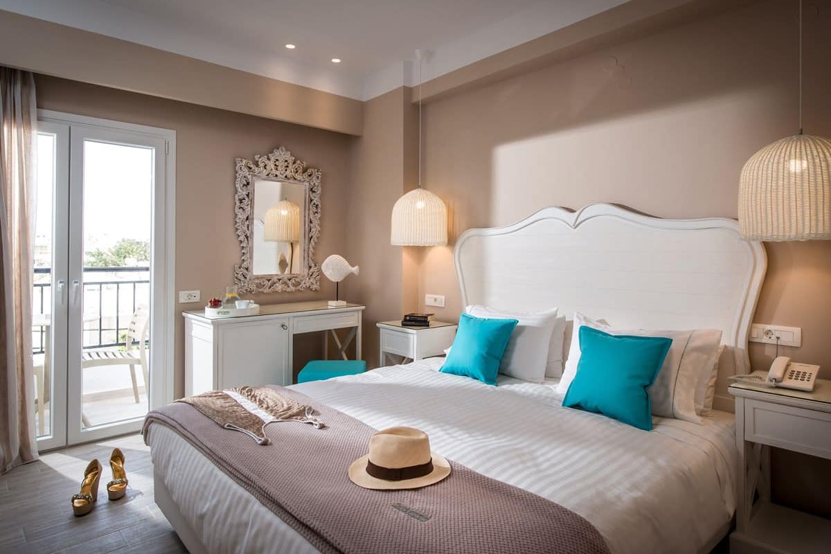 A hotel room with a large bed, a desk, a chair, a mirror, and a balcony.