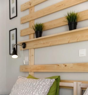 A bedroom with wooden headboard shelves, two potted plants, a bedside lamp, and a patterned pillow.