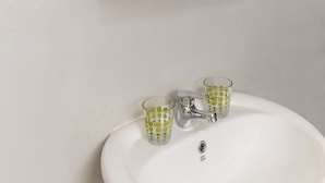 Un baño con espejo, toallero y lavabo con dos vasos.