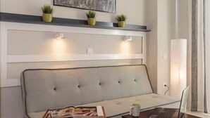 Una sala de estar moderna con un sofá gris, una mesa de centro, una computadora portátil y una revista. Hay tres macetas con plantas en un estante sobre el sofá.