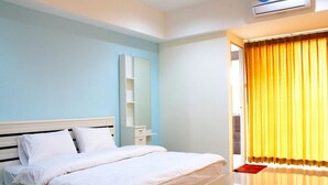 Un dormitorio con cama, mesita de noche, espejo y ventana con cortinas amarillas.