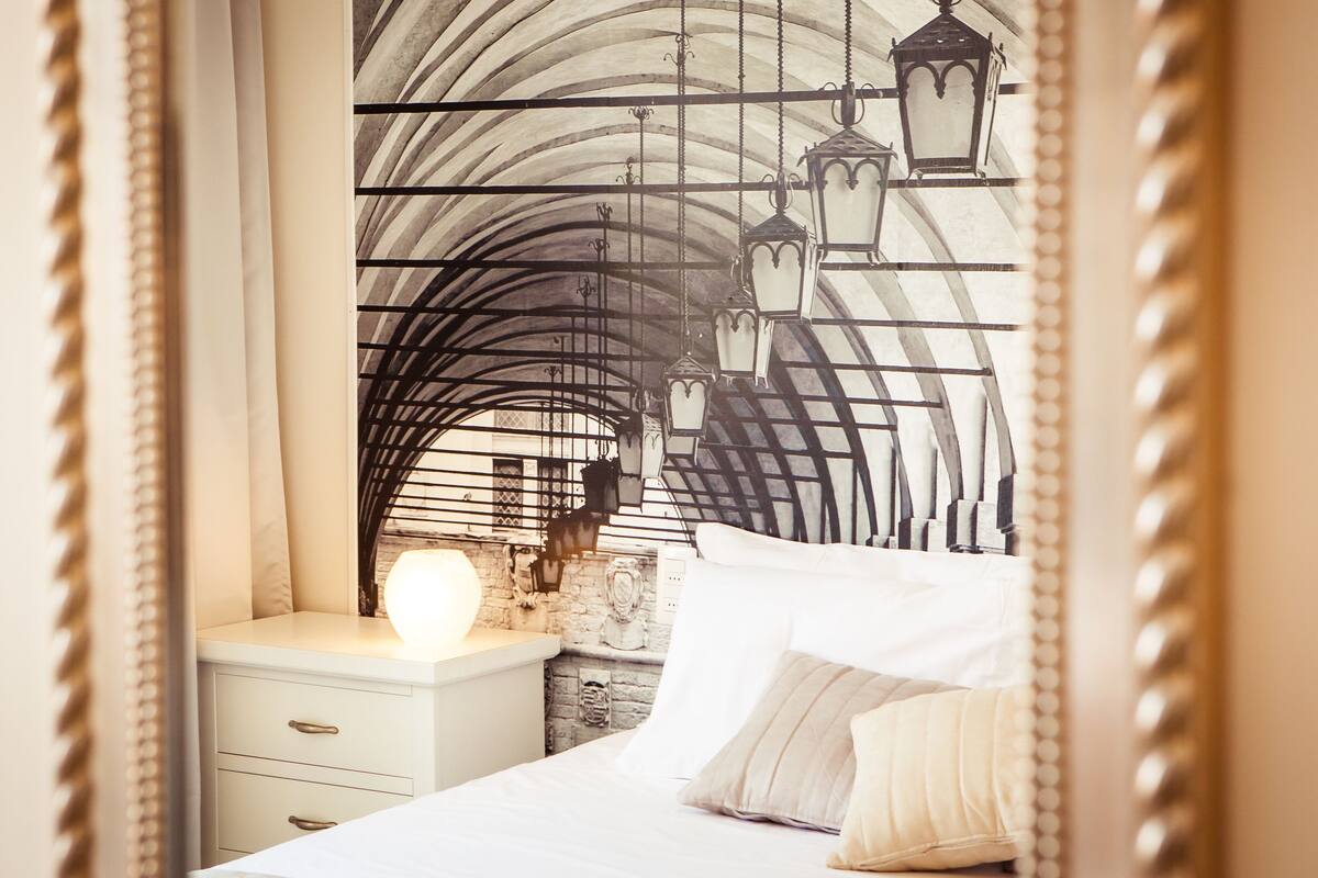 Un dormitorio con una cama, una mesita de noche y una pared con un arco de metal decorativo y faroles colgantes.