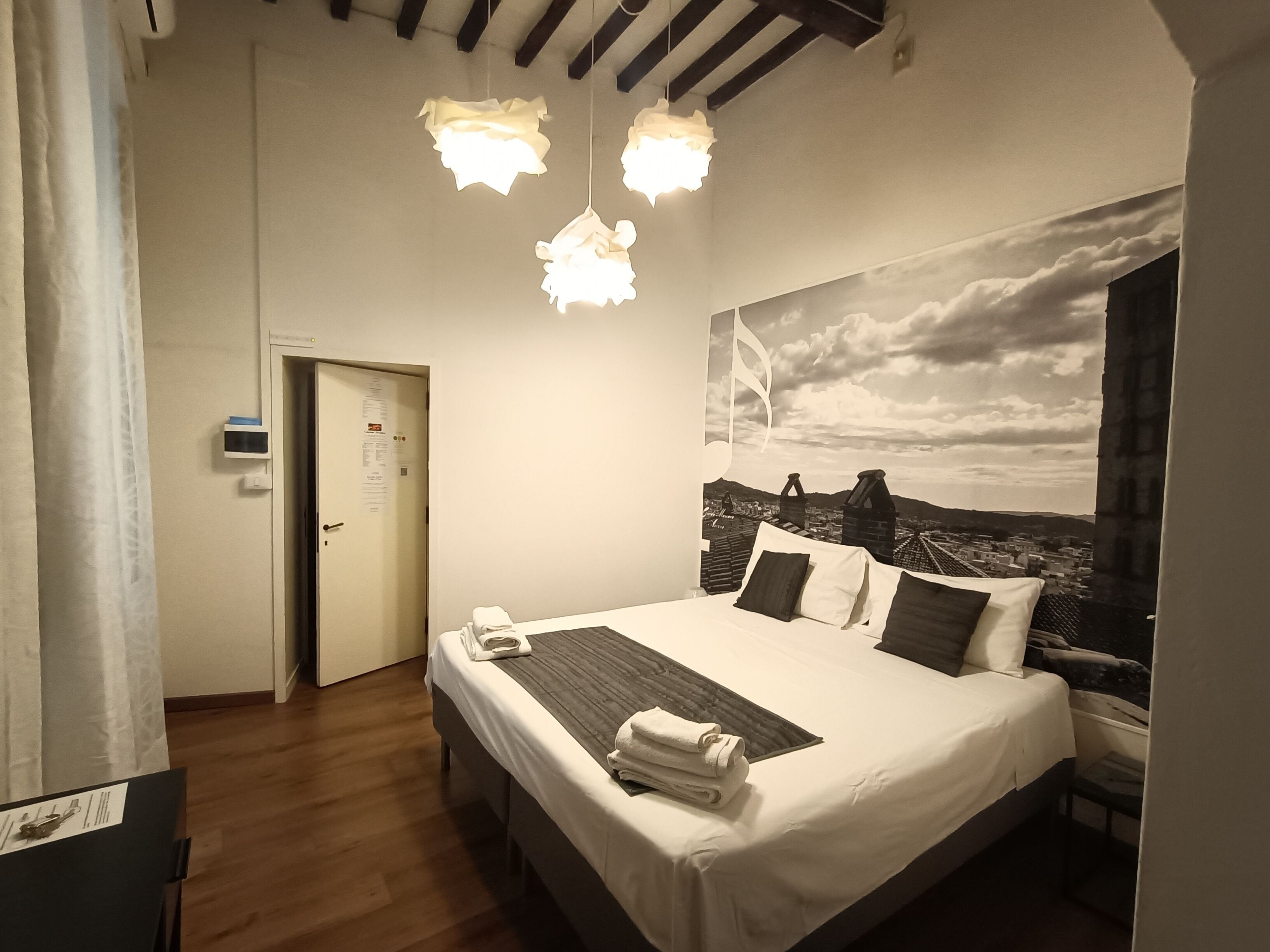 A hotel room with a bed, a view of the cityscape, and a ceiling with exposed beams.