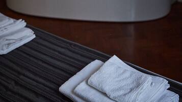 A bathtub with blue lighting, a wooden bench with folded towels, and a dark wooden floor.