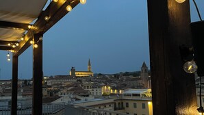 Une terrasse sur le toit, agrémentée de guirlandes lumineuses, de plantes en pot et offrant une vue sur le paysage urbain, avec ses bâtiments historiques.