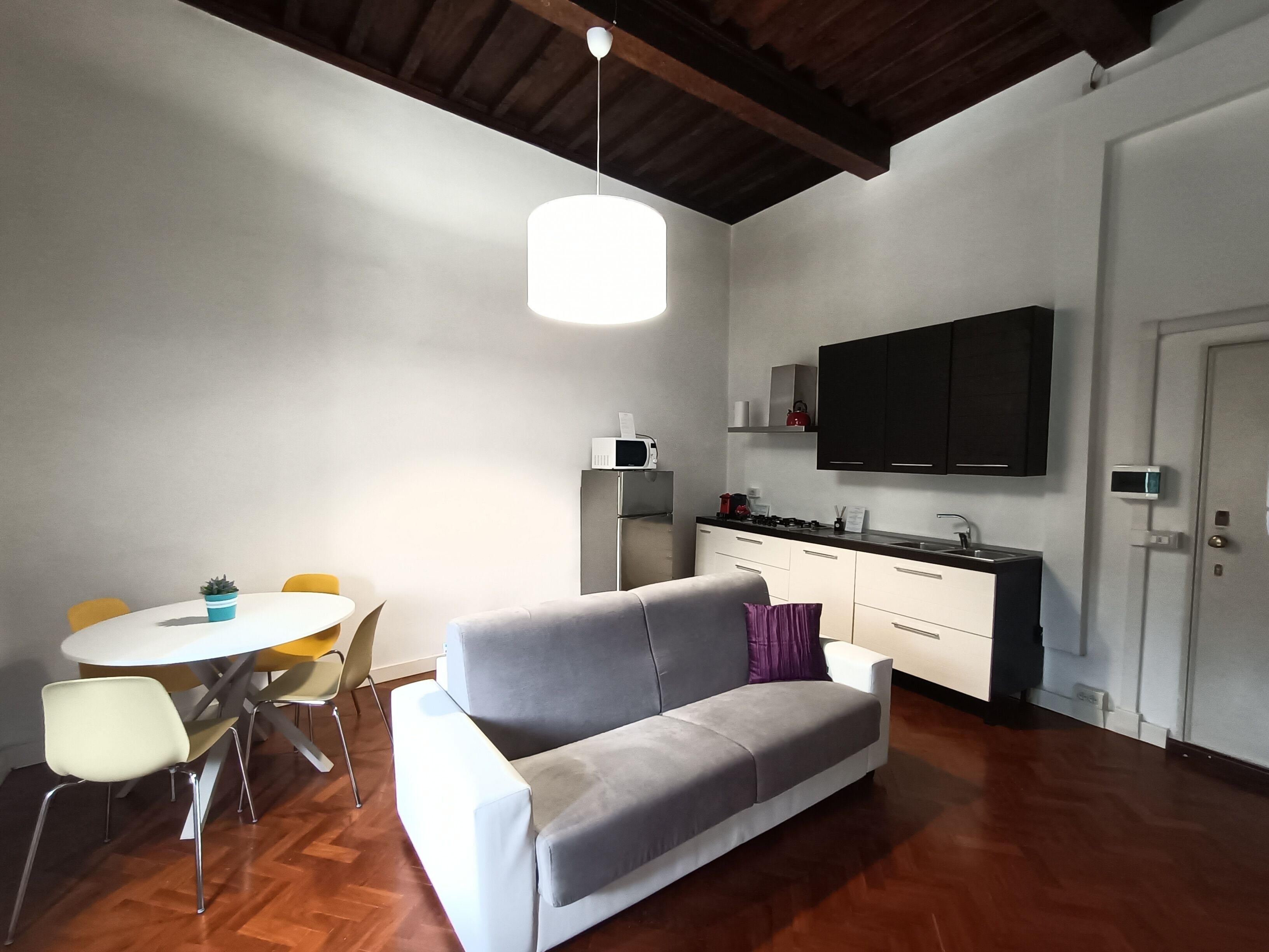 Un espacio habitable moderno con un sofá gris, una mesa de comedor con sillas, una zona de cocina con estufa y microondas, y un televisor de pantalla plana grande montado en la pared.