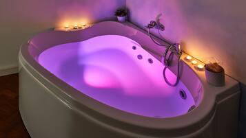 A modern bathtub with a built-in water jet system, surrounded by candles and a potted plant, creating a relaxing ambiance.
