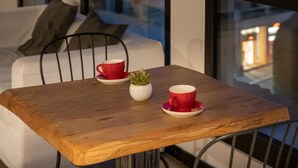 Une pièce chaleureuse avec une table en bois, deux tasses rouges, une petite plante et une vue sur le paysage urbain, visible à travers de grandes fenêtres.