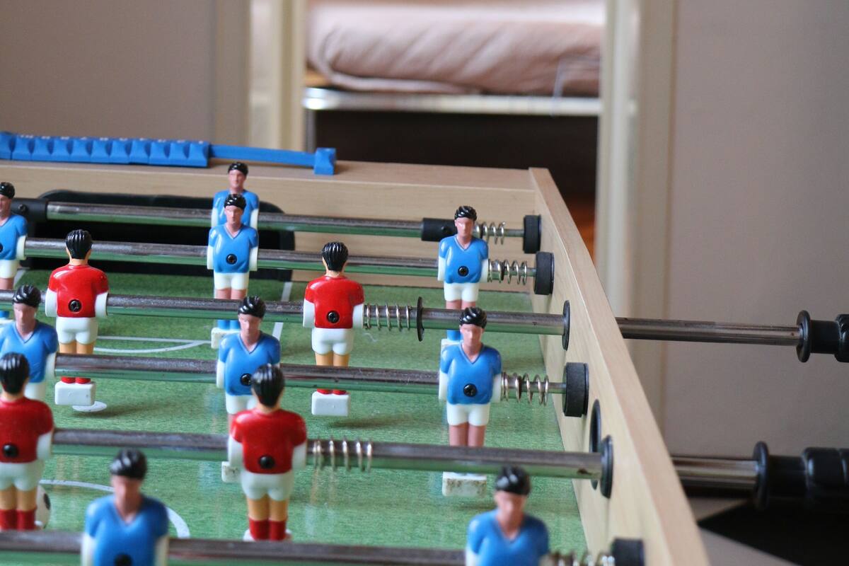 Una mesa de fútbolín en una habitación con una cama y una ventana al fondo.
