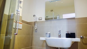 Un baño con cabina de ducha de vidrio, un lavabo blanco con espejo y un perchero con una toalla negra.