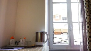 Una encimera de cocina con una tetera, tazas y una ventana que ofrece vistas a edificios.