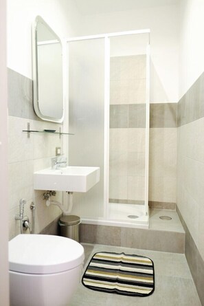 A bathroom with a white sink, a mirror, a shower enclosure, and a striped bath mat. - Your Rome (Rome)
