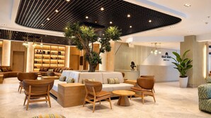 Een moderne hotelentree met een centraal zithoekje, een receptiebalie en een grote kamerplant.