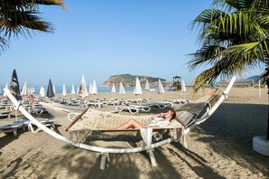 Una playa con una hamaca, sillas de descanso y sombrillas.