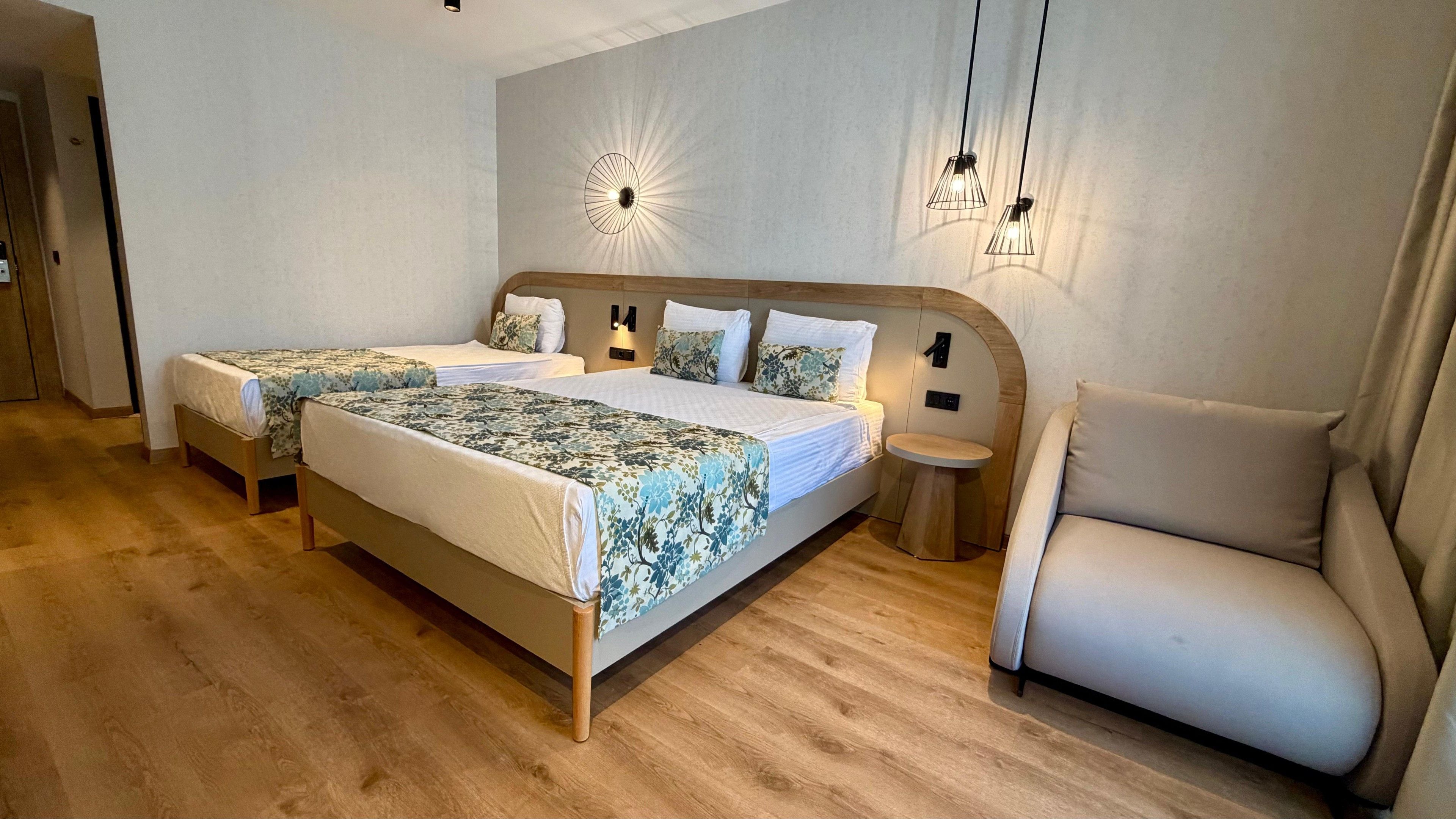 A double bed with a floral bedspread, a bedside table, a chair, and a wall-mounted light fixture.