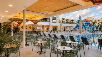 A poolside area with lounge chairs and tables, a pool, and a children's play area.